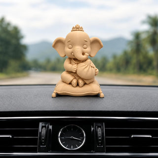 Mini Ganesha idol in sand finish seated on a cushion, on a car dashboard